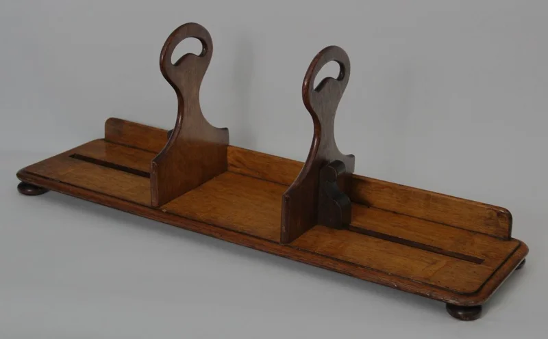 Draagbare boekenstand - Diversen › Varia - €295.00 - Draagbare boekenstand die oorspronkelijk gebruikt werd in leeszalen van bibliotheken. Met deze boekenstand kon men een serie boeken ophalen en naar de leestafel dragen. De twee steunen zijn verschuifbaar om de boeken samen te houden. De steunrand achteraan belet dat de boeken uit de drager schuiven.
Gemaakt in eik.
70cm lang, 20cm diep, steunen 28cm hoog.
Victoriaanse periode, late 19e eeuw.