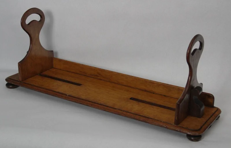 Draagbare boekenstand - Diversen › Varia - €295.00 - Draagbare boekenstand die oorspronkelijk gebruikt werd in leeszalen van bibliotheken. Met deze boekenstand kon men een serie boeken ophalen en naar de leestafel dragen. De twee steunen zijn verschuifbaar om de boeken samen te houden. De steunrand achteraan belet dat de boeken uit de drager schuiven.
Gemaakt in eik.
70cm lang, 20cm diep, steunen 28cm hoog.
Victoriaanse periode, late 19e eeuw.