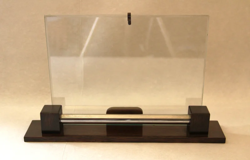 Modernistische fotohouder - Diversen › Varia - €45.00 - Late Art Déco / modernistische fotohouder.
Voetplaat in donker eik en verchroomde dwarsversiering.
Lengte voetplaat: 31cm; hoogte glasplaat: 20cm